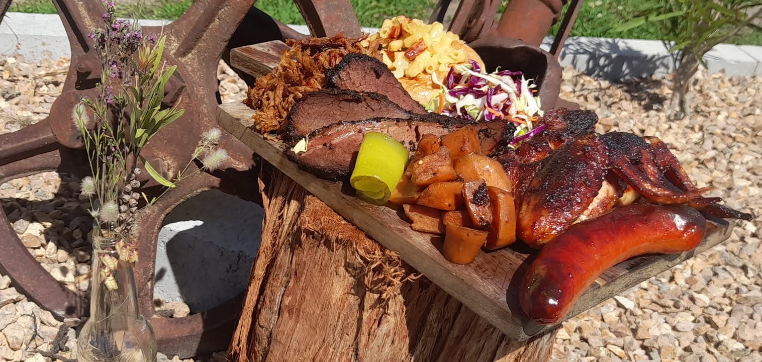 A board of smoked brisket, pulled meat, mac and cheese, coleslaw, glazed wings and a smoked sausage on a tree stump