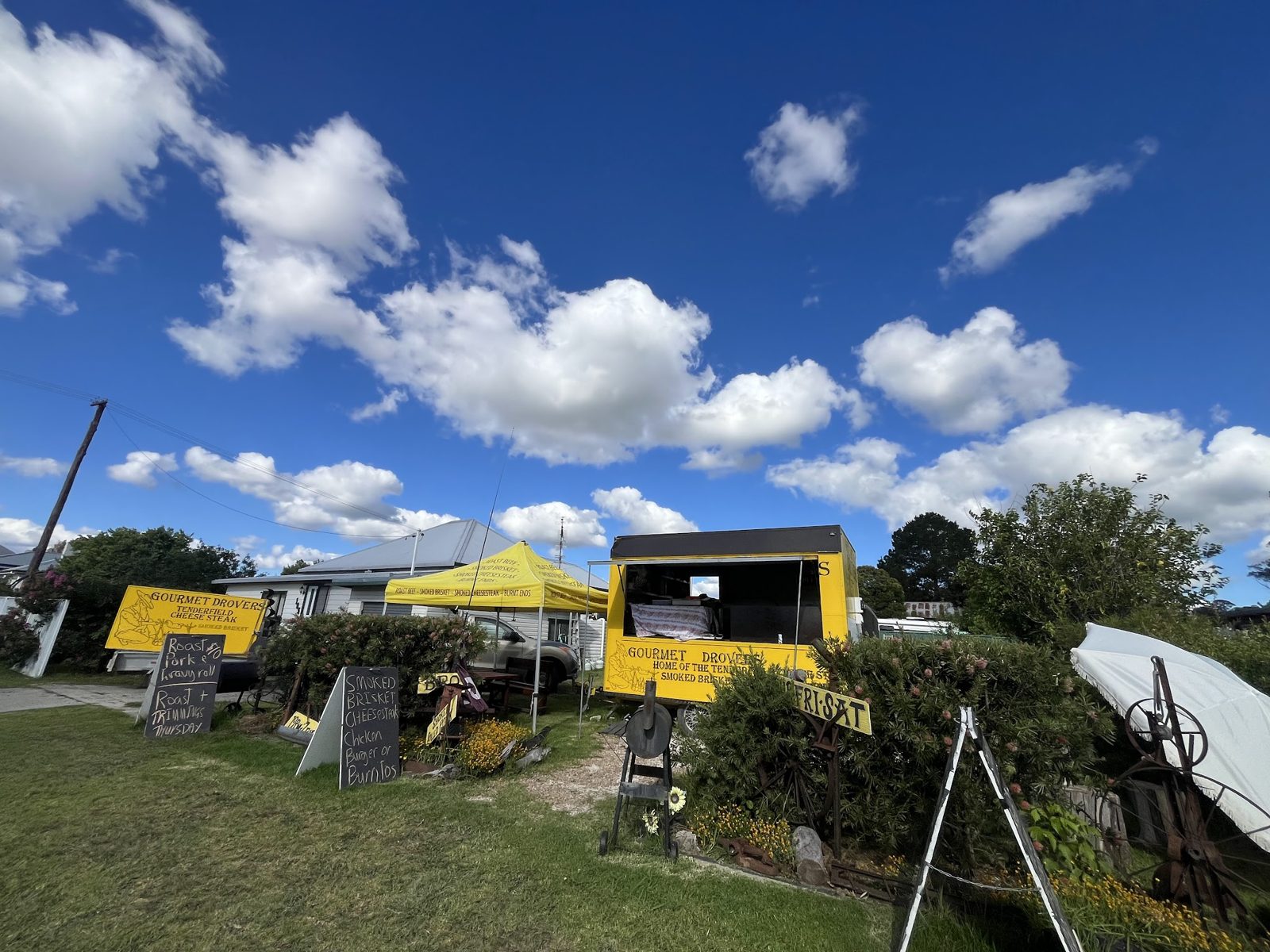 The yellow Gourmet Drovers trailer and signs on the lawn at Rouse Street under a blue sky