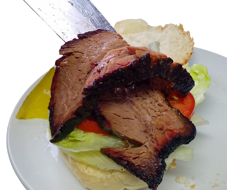 Thick slices of smoked brisket being served onto a roll with lettuce and tomato