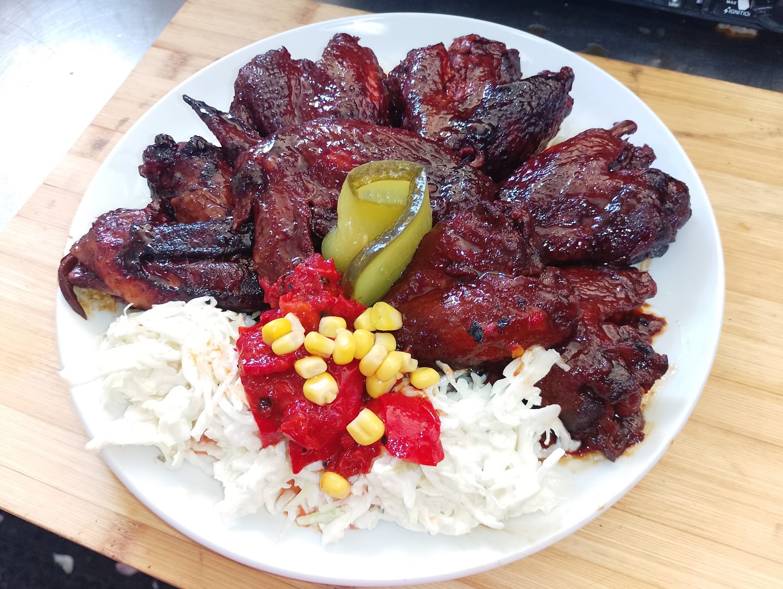 Glazed smoked chicken wings on a white plate with coleslaw, corn and salsa